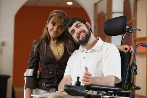 A couple with one man in a wheel chair and a lady standing next to him.