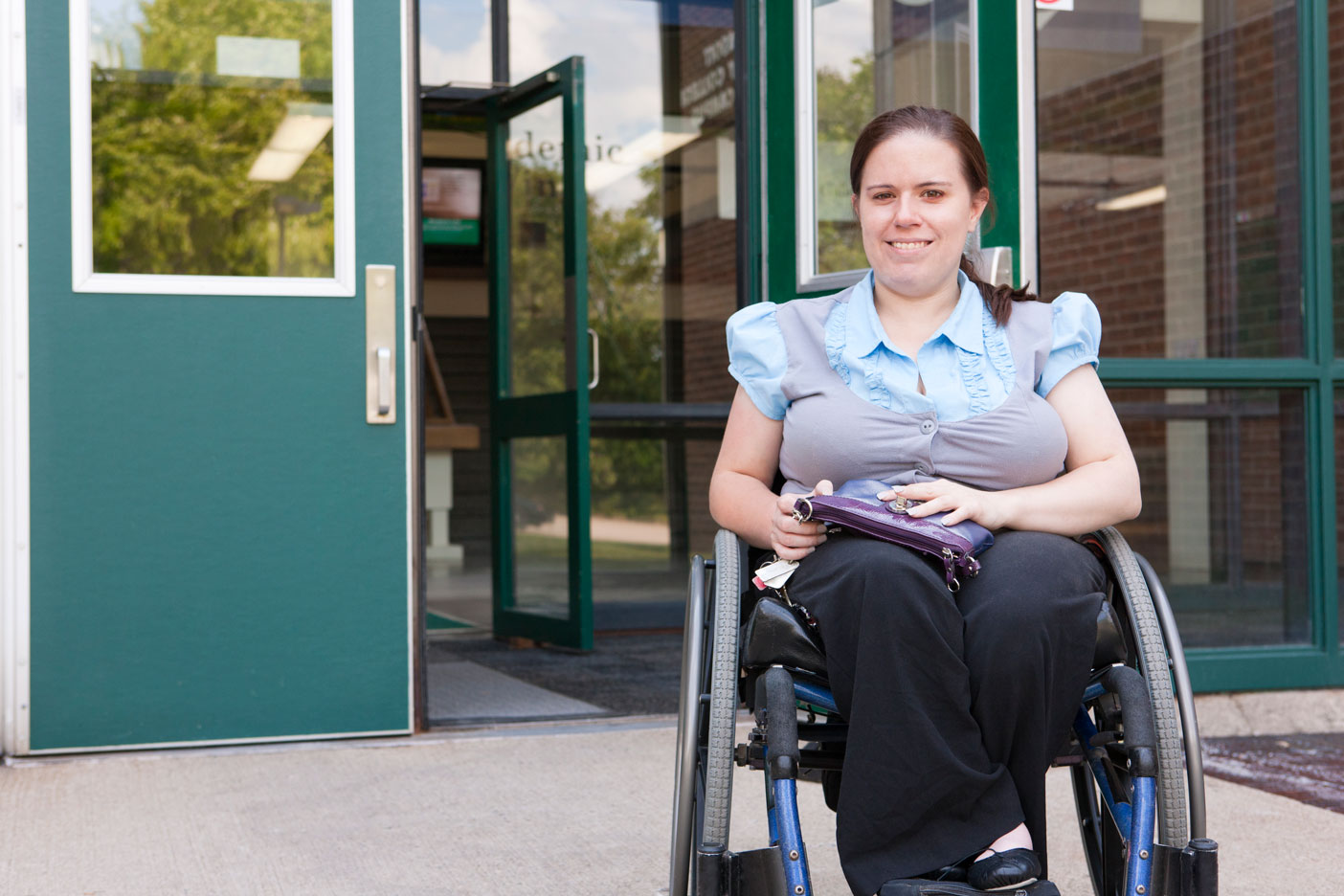 A young lady sitting in a wheel chair outside smiling at you!