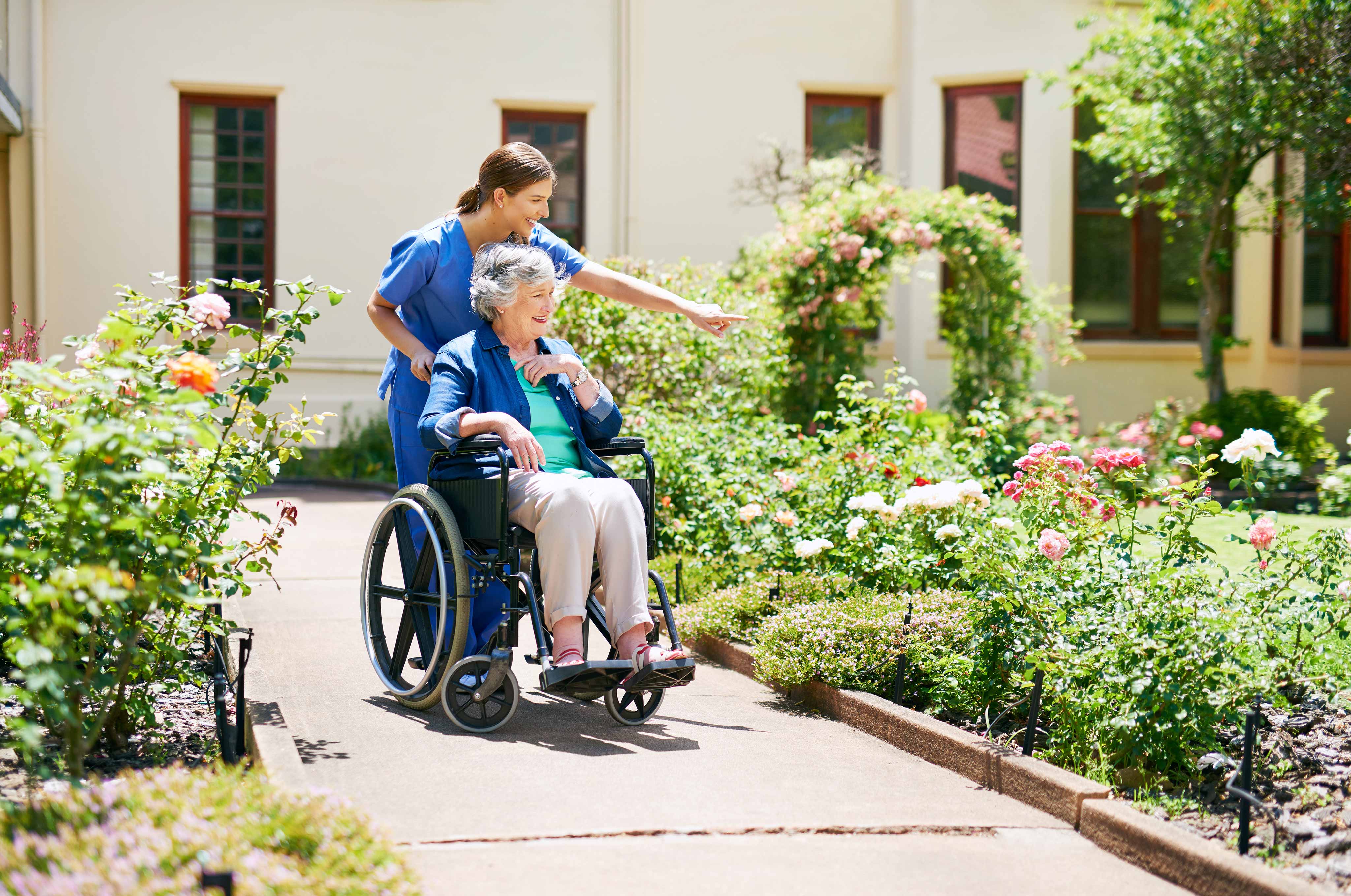 Lady in wheelchair with her caregiver looking at flower in front of a house.